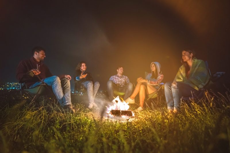 The five happy people rest near a bonfire. evening night time